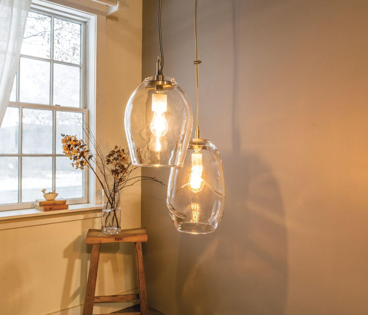 Two clear glass pendant lights with brass fittings hanging from chains against a warm yellow wall.