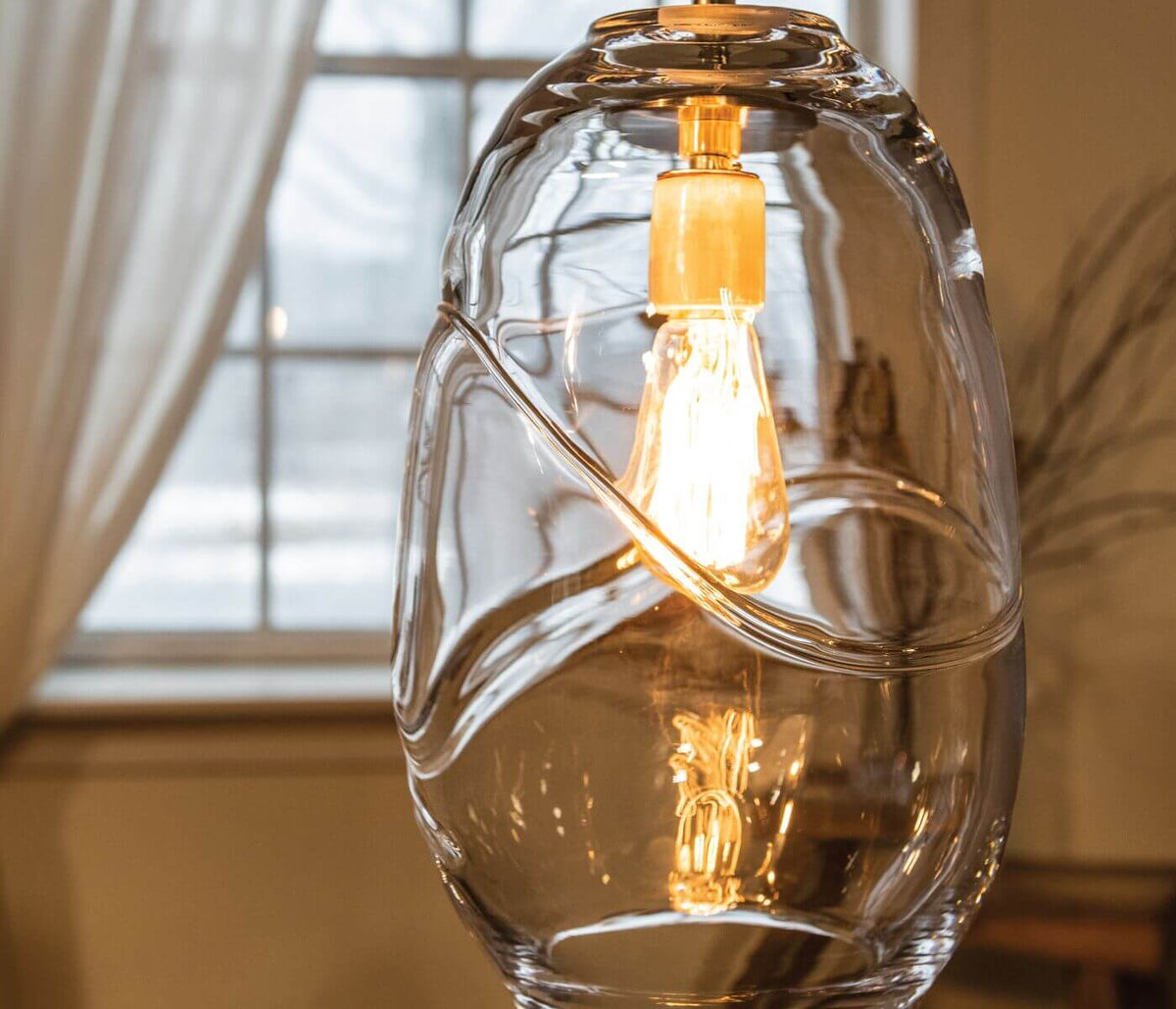 Clear glass pendant with dual filament bulbs suspended inside an organic, asymmetrical dome shade.
