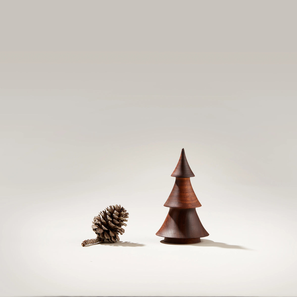 Dark walnut wood evergreen tree sculpture with stacked conical sections next to a pinecone.