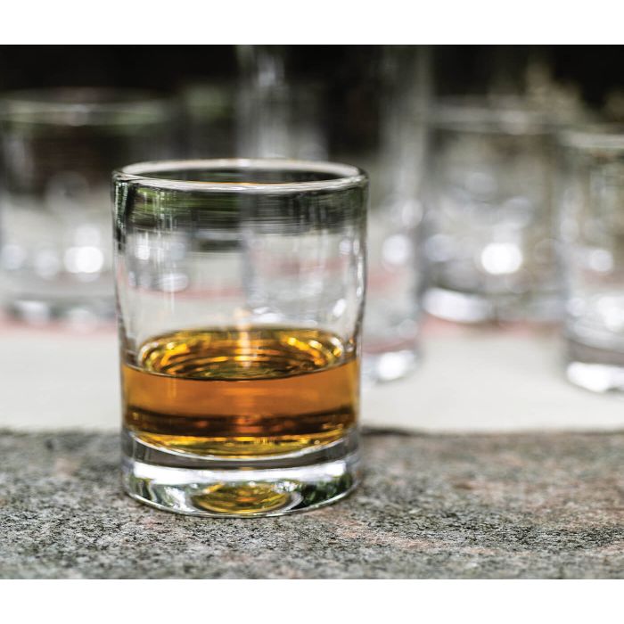 Whiskey glass filled with amber liquid, with additional empty glasses blurred in background.
