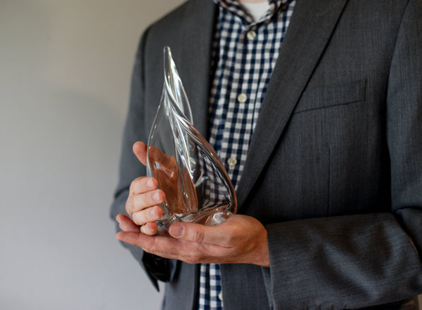 A person in a suit holding a handmade Simon Pearce clear glass award sculpture with a flowing, flame-like form