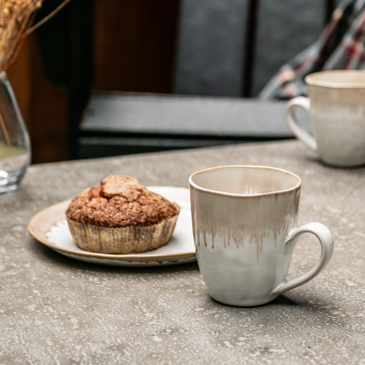 White mug with gray brushstroke pattern and matching plate with muffin on table setting.