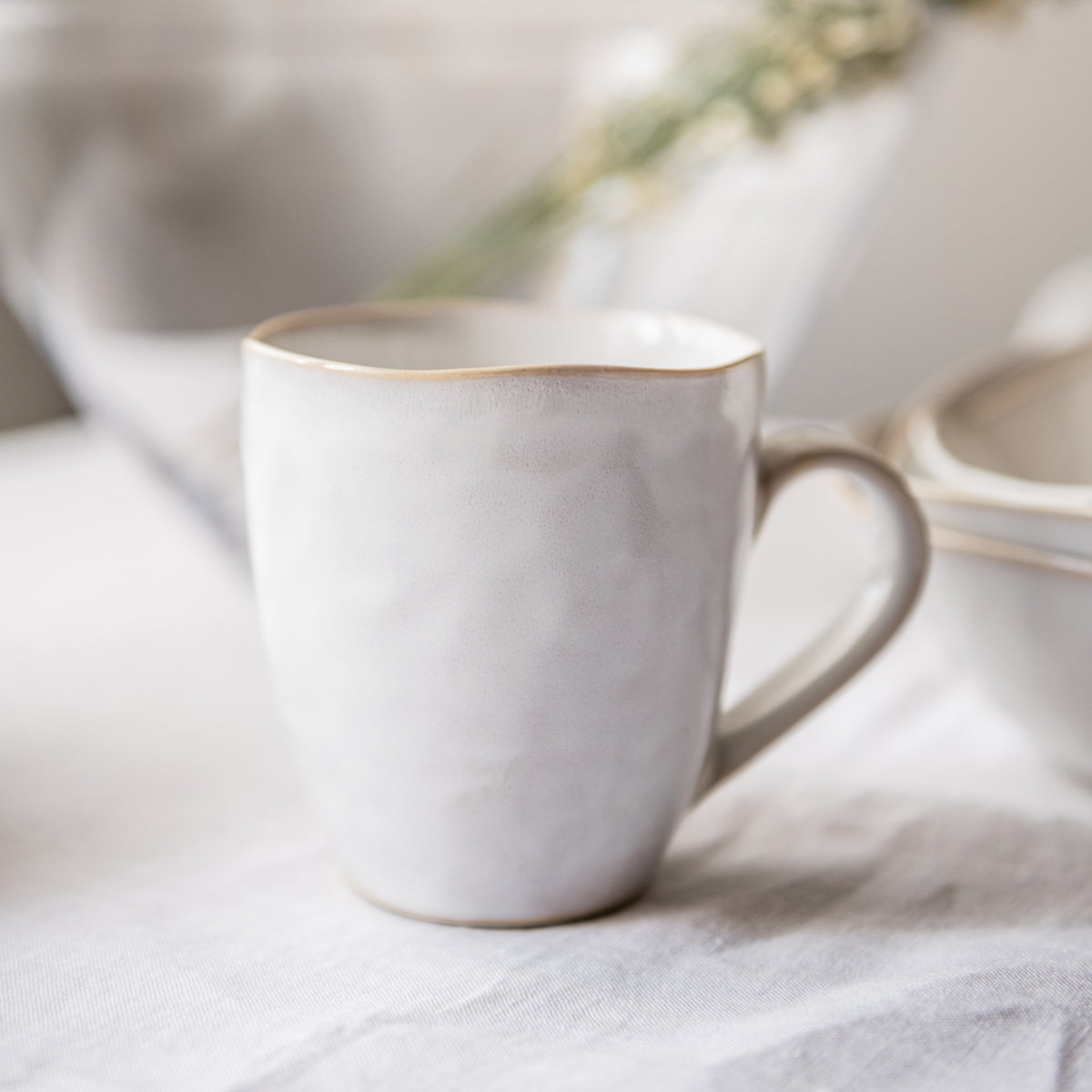 White ceramic mug with tan rim and handle, displayed with matching dinnerware pieces.