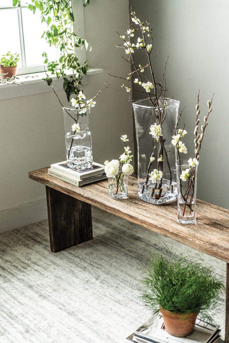 Clear glass cylindrical vase with water and branches of white flowers and pussy willows inside.