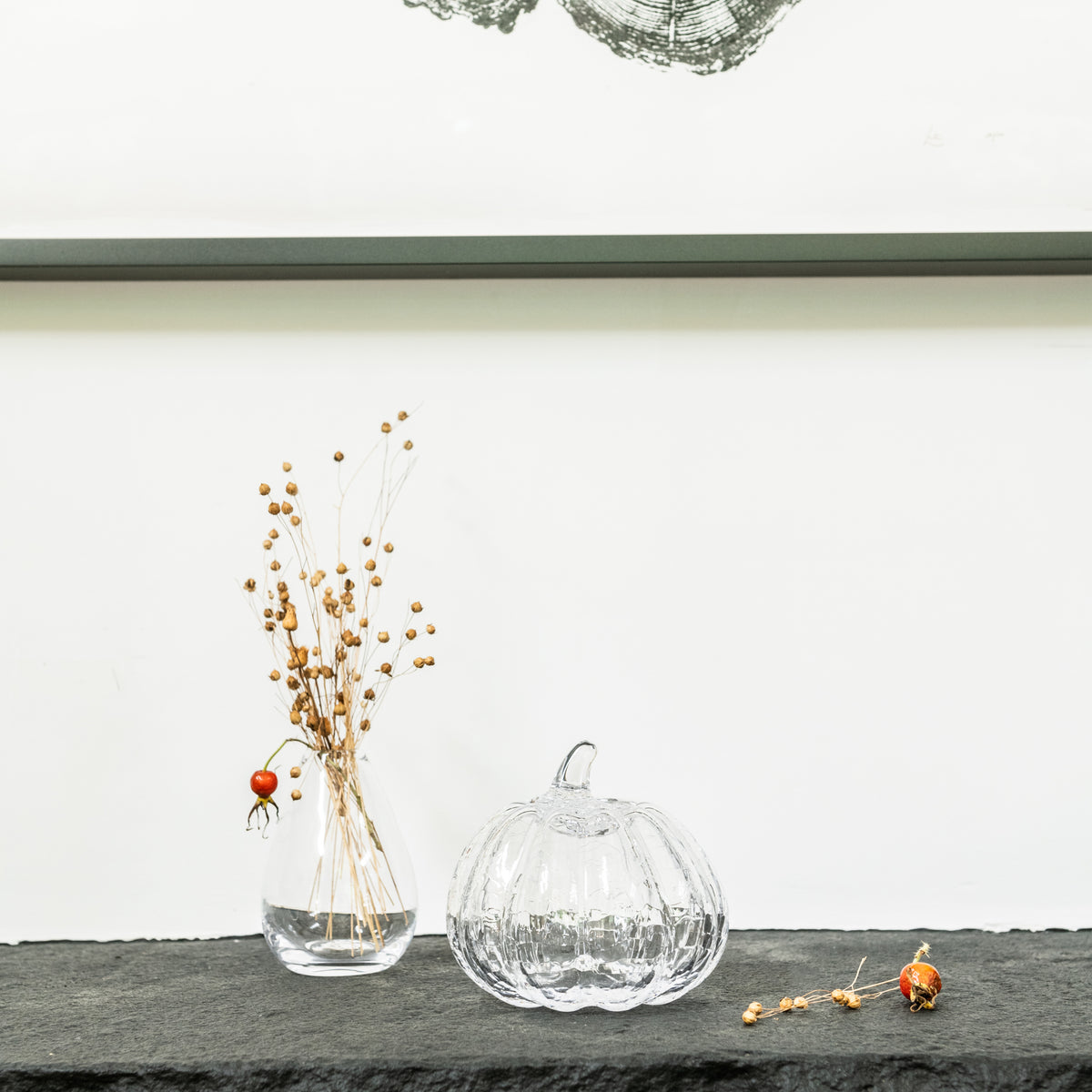 Clear glass pumpkin with crackle texture and stem, displayed next to dried botanicals in a vase.