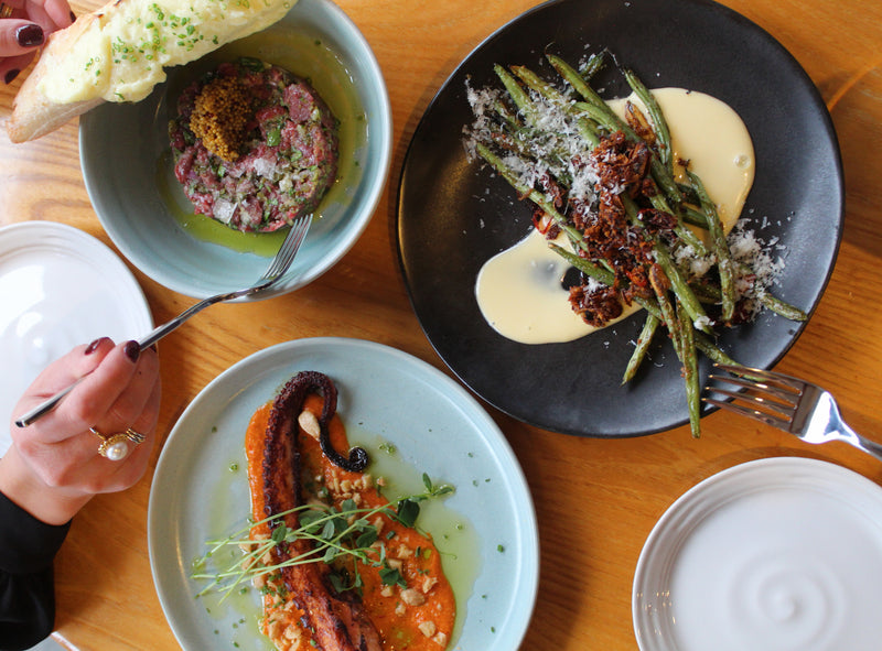 Overhead view of shared plates at Simon Pearce Restaurant, including beef tartare, charred green beans, and grilled octopus
