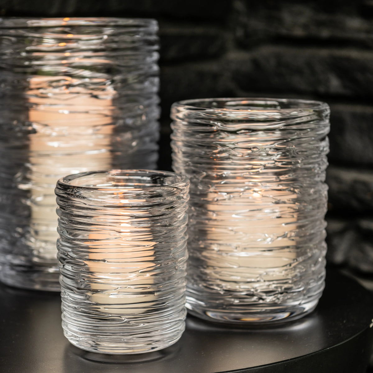 Three clear glass hurricane candles with textured swirl pattern, lit with warm flames inside.