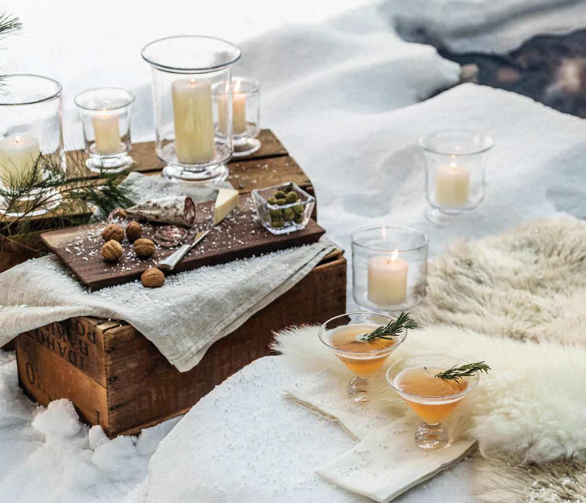Dark wood live edge board with glass bowls containing nuts and greenery, paired with glass candle holders and cocktail glasse
