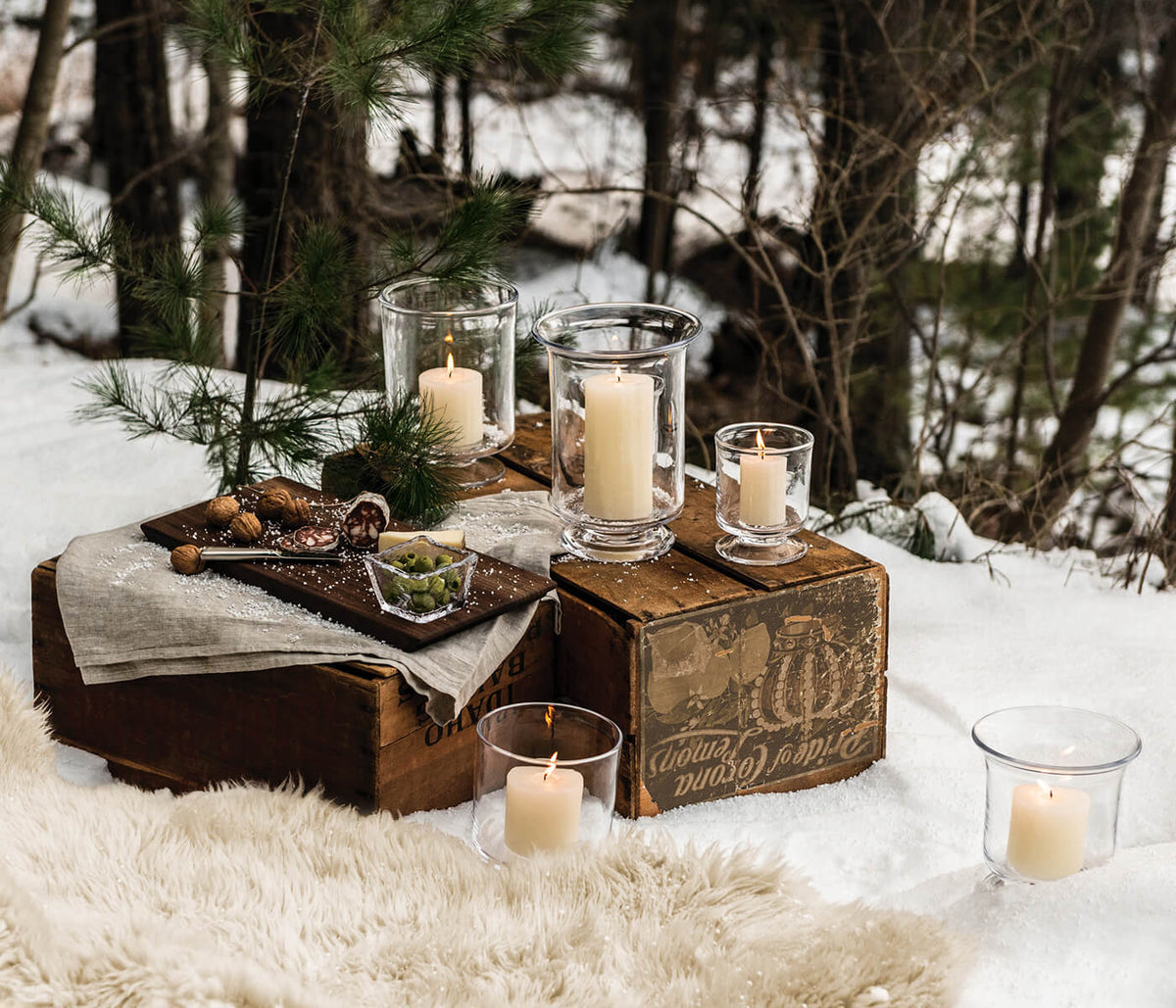 Black walnut live edge board with glass bowl candleholders and lit candles displayed in snowy forest setting.