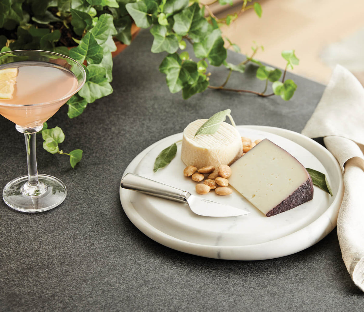 White marble round cheese board with veined surface, displayed with cheese, nuts, and a cheese knife.