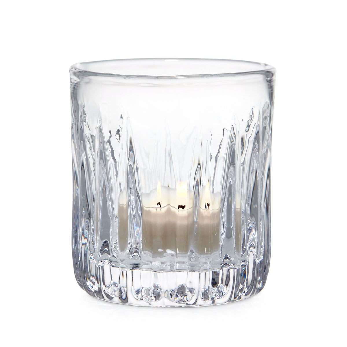 Clear glass tealight holder with vertical ribbed pattern containing lit cream-colored candle.