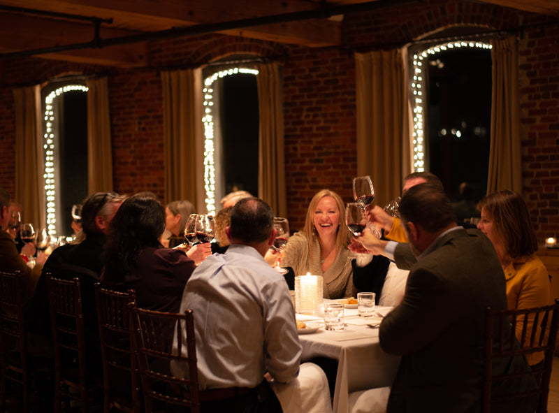 Guests gathered around a candlelit table in the Simon Pearce private dining room, raising glasses of red wine in a toast