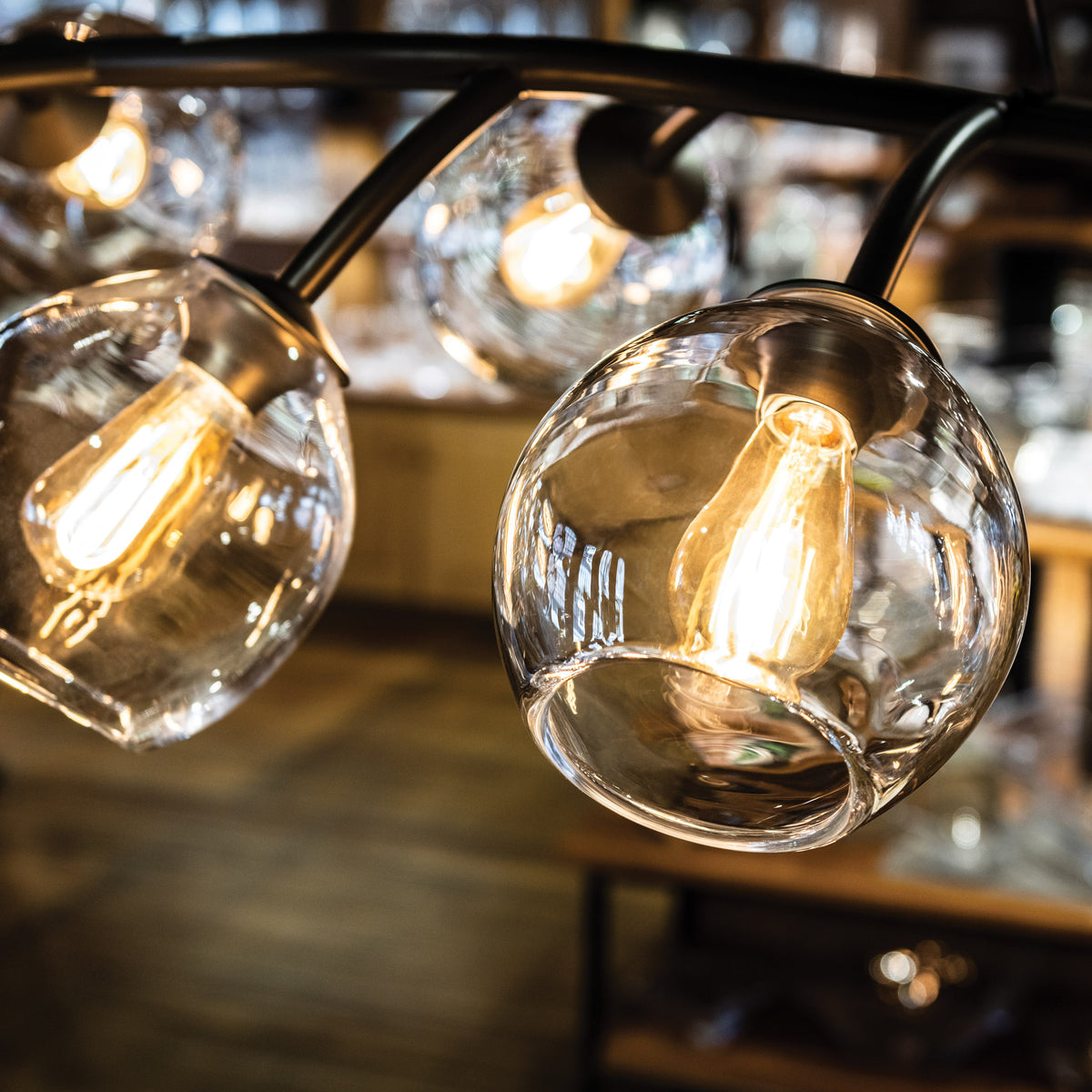 Black metal chandelier with multiple clear glass globe shades and warm-toned Edison-style bulbs.