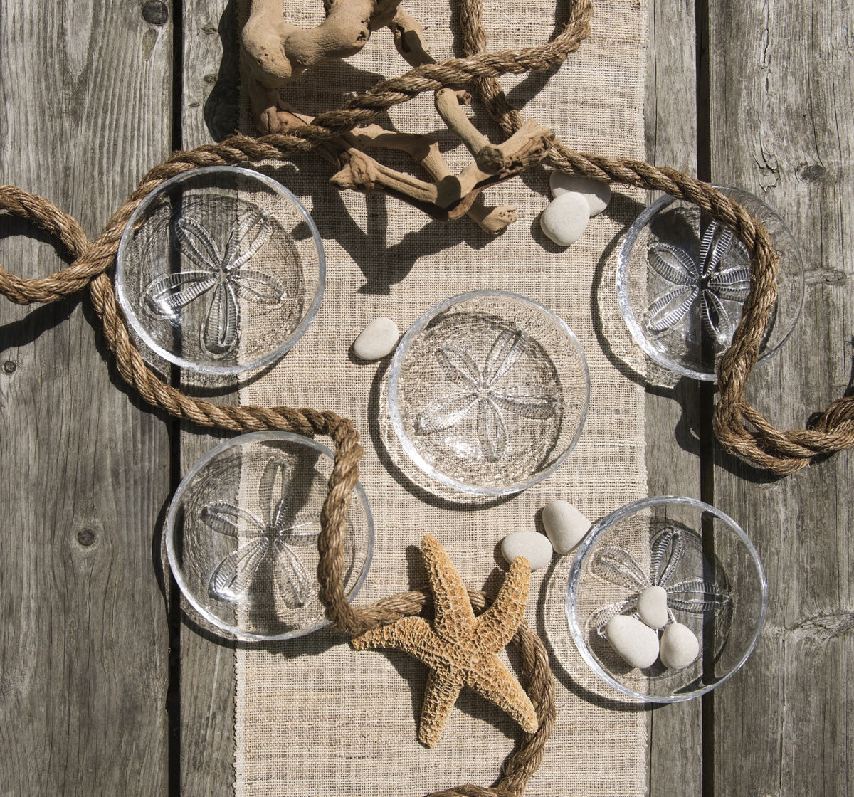 Clear glass bowls with sand dollar etchings, rope handles, displayed with starfish and white shells on linen.