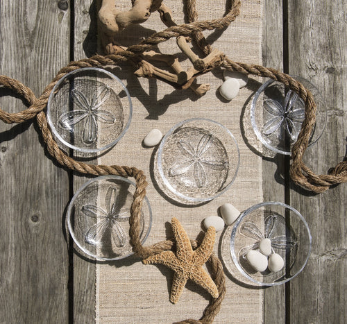 Clear glass bowls with sand dollar etchings, rope handles, displayed with starfish and white shells on linen.