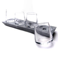 Four clear whiskey glasses arranged on a gray soapstone base with circular indentations.