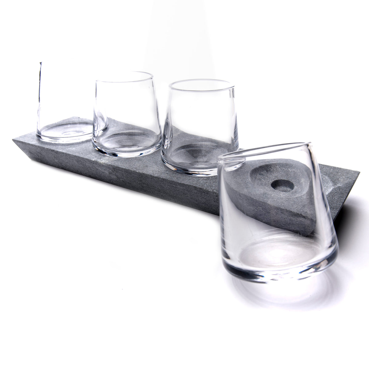 Four clear whiskey glasses arranged on a gray soapstone base with circular indentations.
