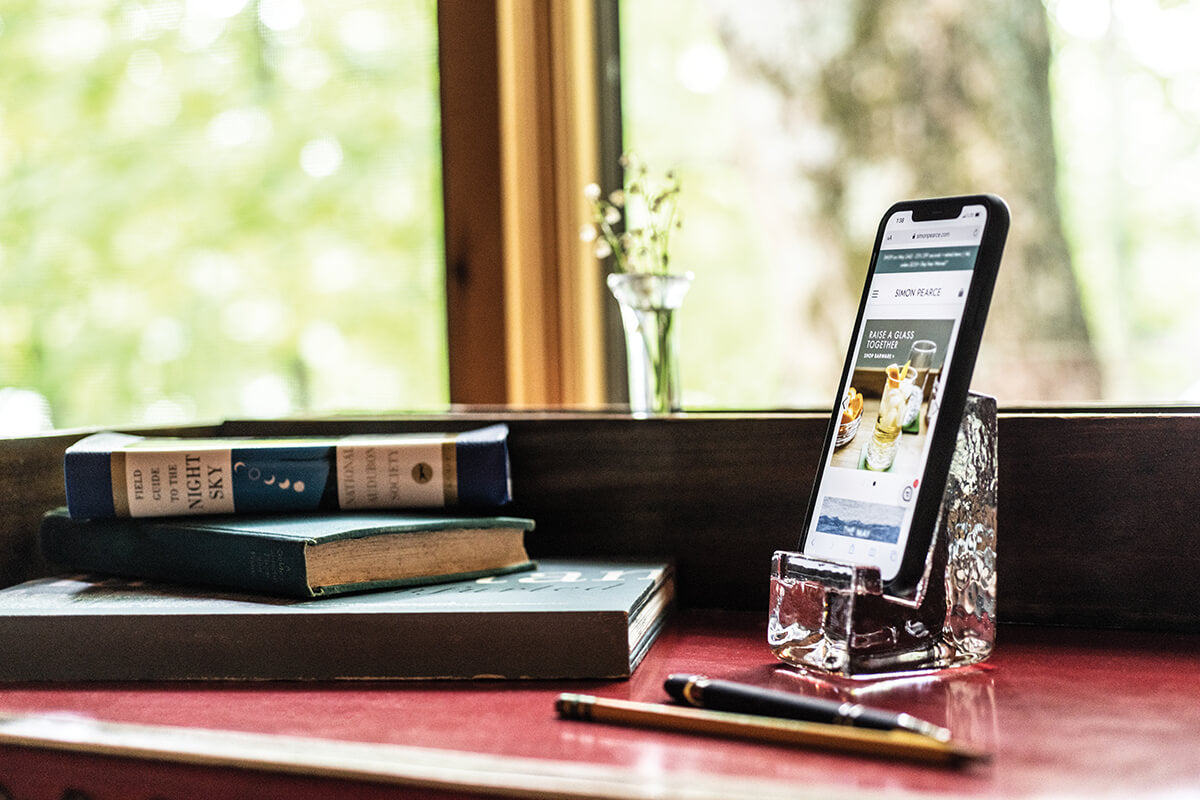 Clear acrylic phone holder displaying smartphone on desk with books and pen nearby.