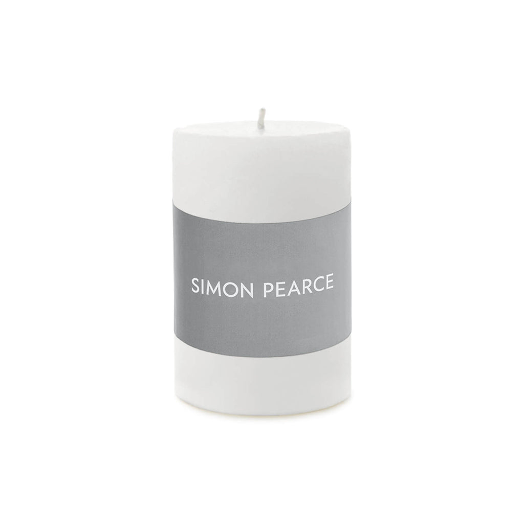 White cylindrical pillar candle with gray band labeled "SIMON PEARCE" and visible wick on top.